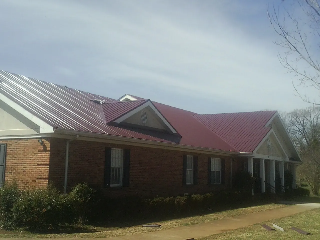 Red metal roof with gabled entries on a long brick building, from a Hail Damage Roof Repair job in Custer