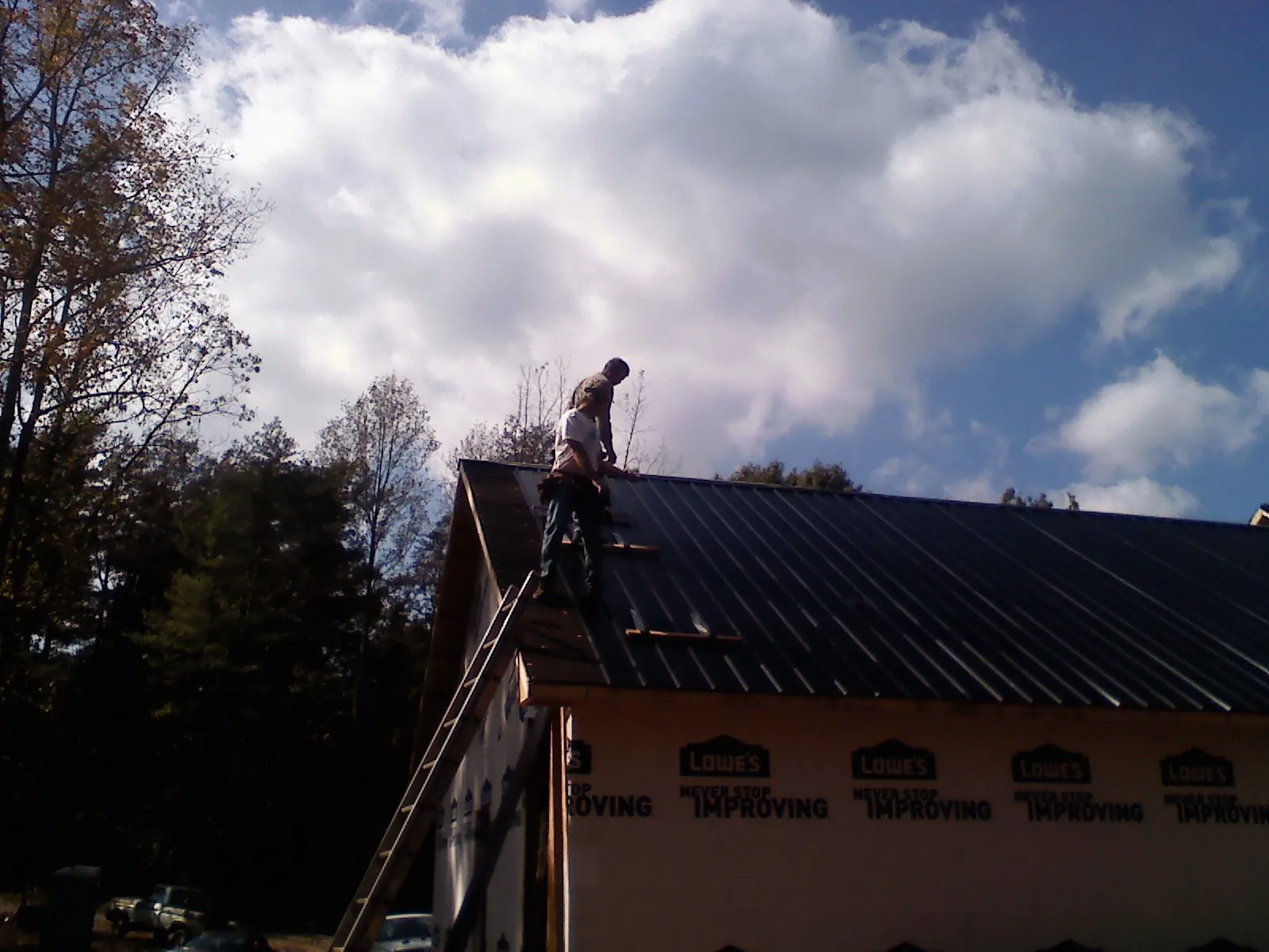 Roofer fastening dark metal panels high against a cloudy sky, from a Roof Inspection job in Custer