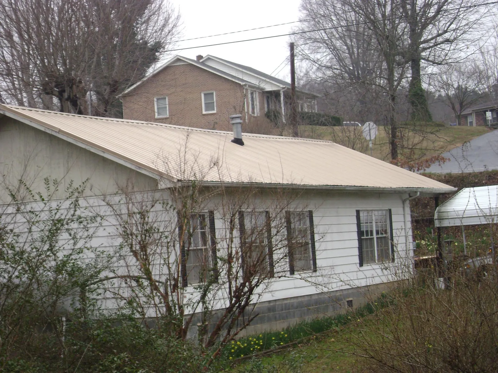 Tan metal roof on a white sided house set into a hillside — Commercial Roofing by Roofing Brothers in Custer