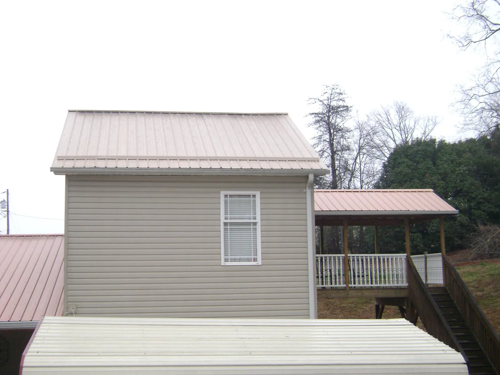 Tan metal roofs on a two story addition and attached porch, from a Roof Replacement job in Custer